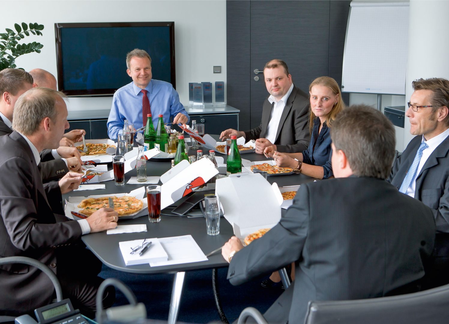 Dr. Jens Baas, TK-Vorstandsvorsitzender (Mitte), mit Mitarbeitern beim Pizza-Treff. Pressefoto der Techniker Krankenkasse zur Verwendung für redaktionelle Zwecke.