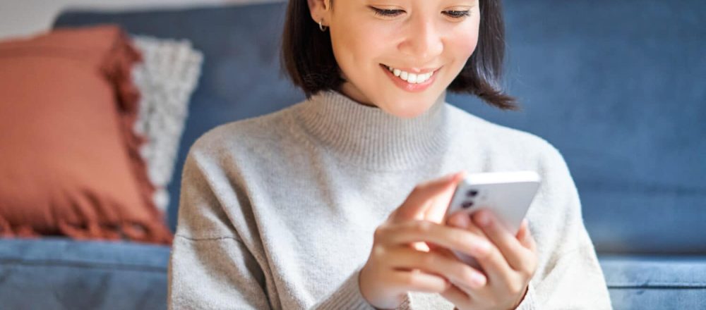 Smiling woman using her mobile phone at home, illustrating a seamless omnichannel insurance customer experience
