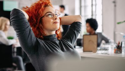 Businesswoman resting after work and day dreaming in the office. There are people in the background.